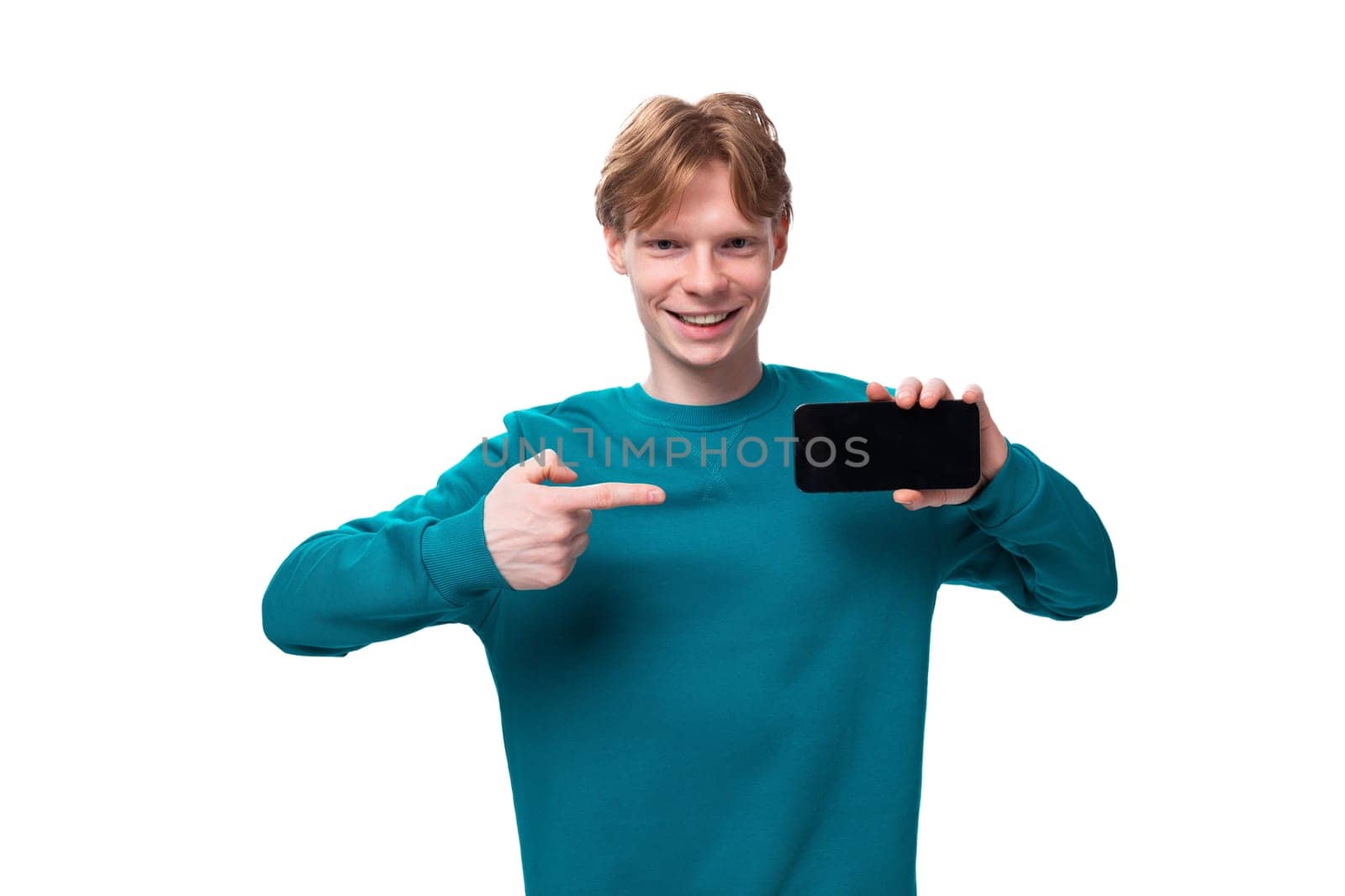 young handsome red-haired man with a blue sweater points a finger at a smartphone.