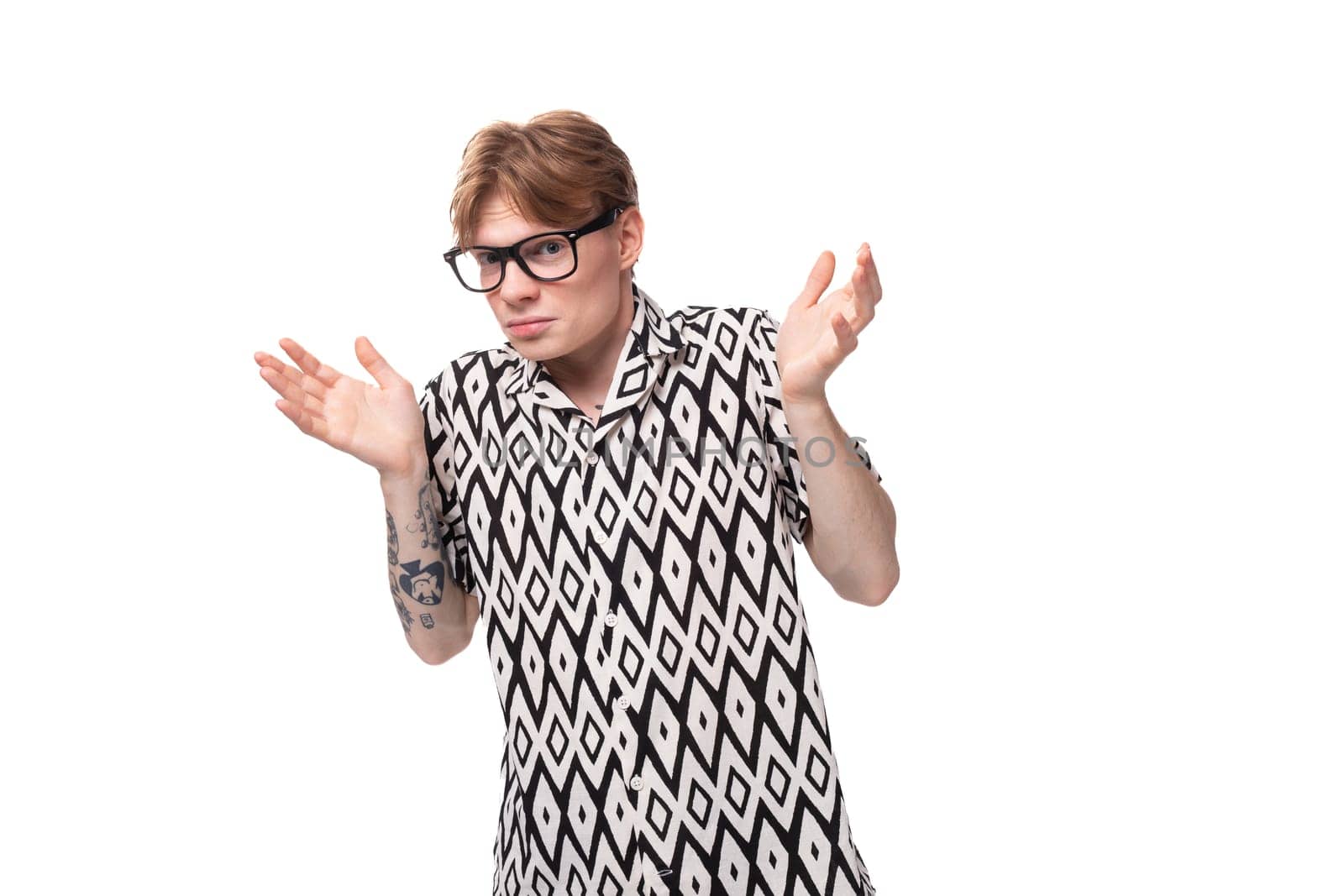 European young man with golden hair and a tattoo on his arms dressed in a summer black and white shirt is experiencing discomfort from wearing glasses by TRMK