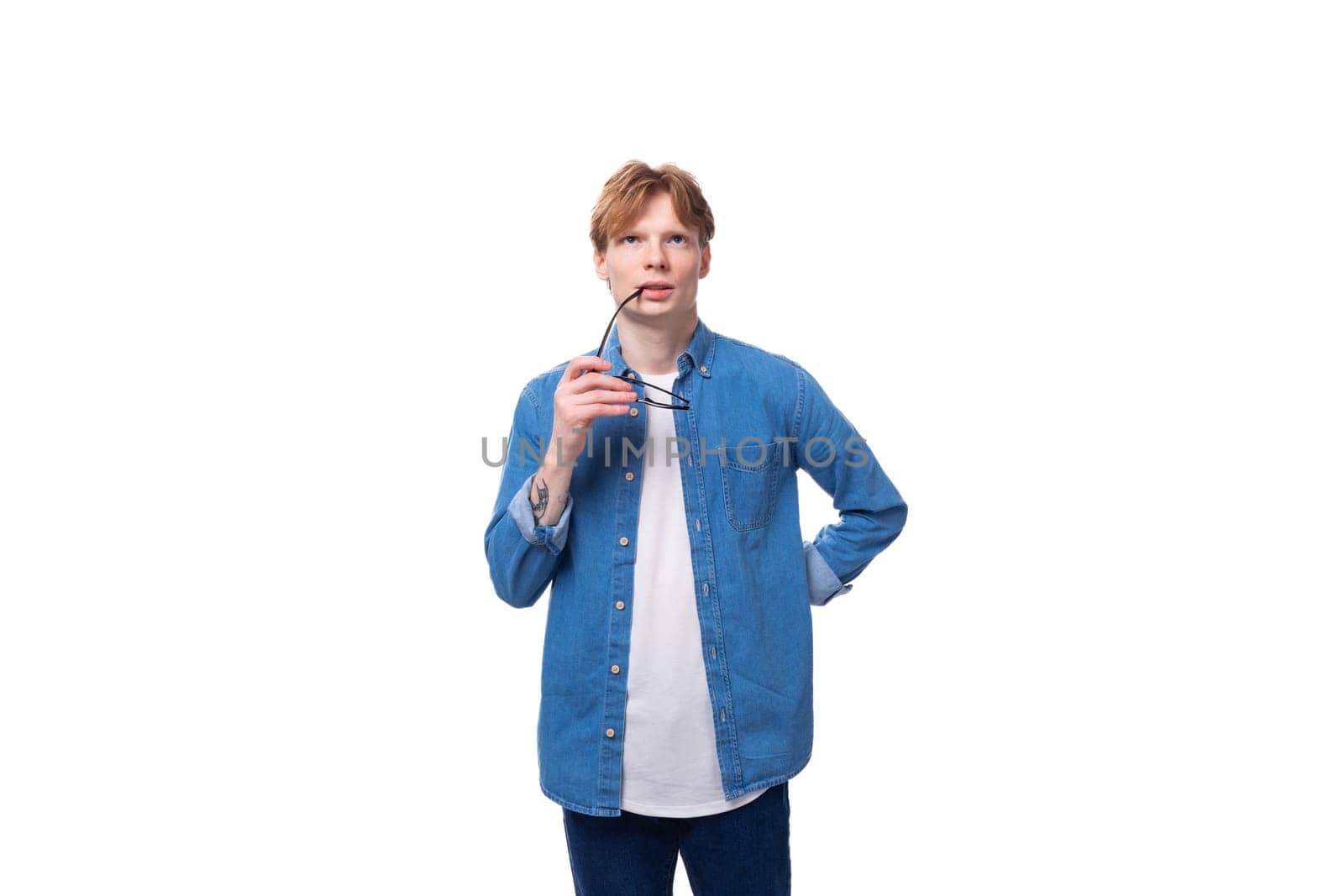 young smart european man with copper hair wears denim shirt thoughtfully holds glasses by TRMK