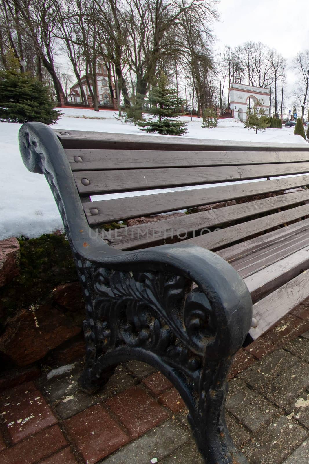 Outdoor bench made of wood placed on brick sidewalk close up