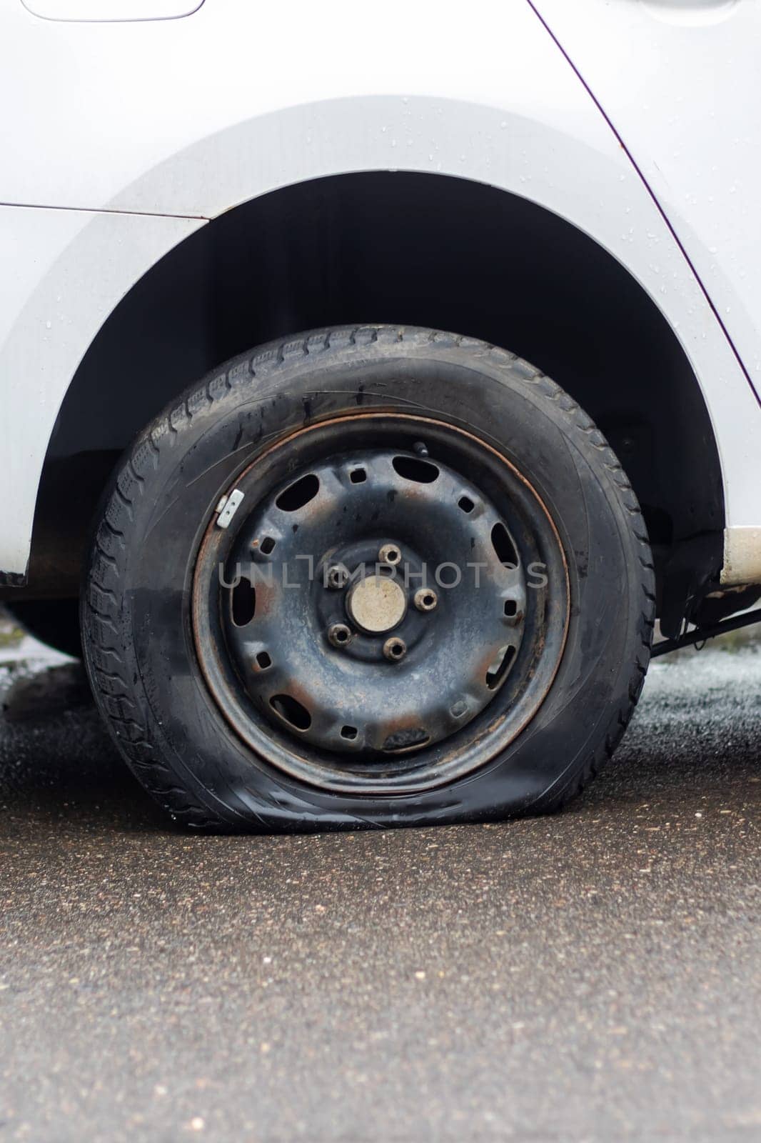 A car with a flat automotive tire on the side of the road, showing its alloy wheel and locking hubs. The tread made of synthetic rubber is visible, with the hubcap missing