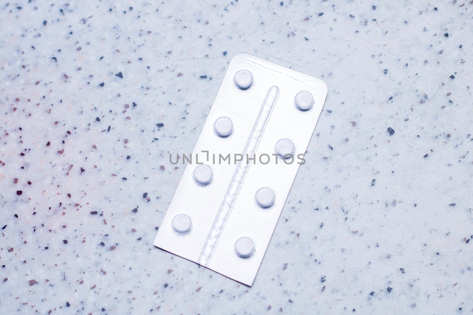 A rectangular blister pack of pills with a circle pattern in electric blue on a plastic sleeve. It sits on a metal counter top, resembling a fashionable accessory