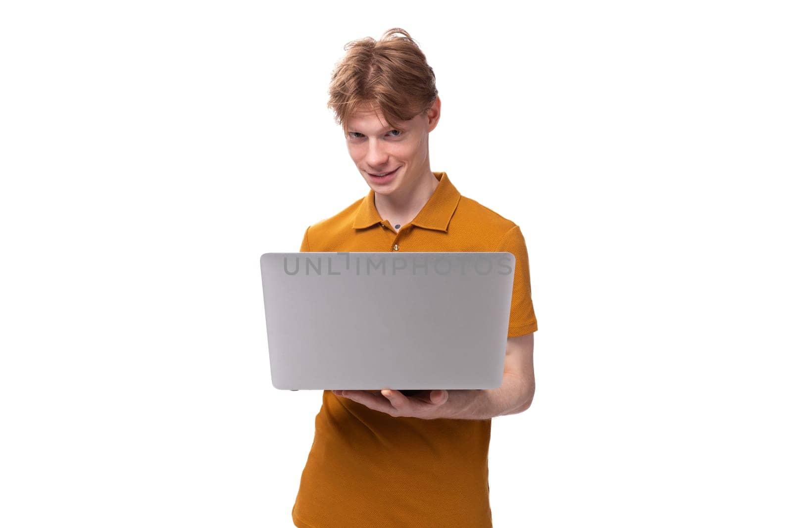 young red-haired guy in an orange t-shirt is studying using a laptop on a white background with copy space by TRMK