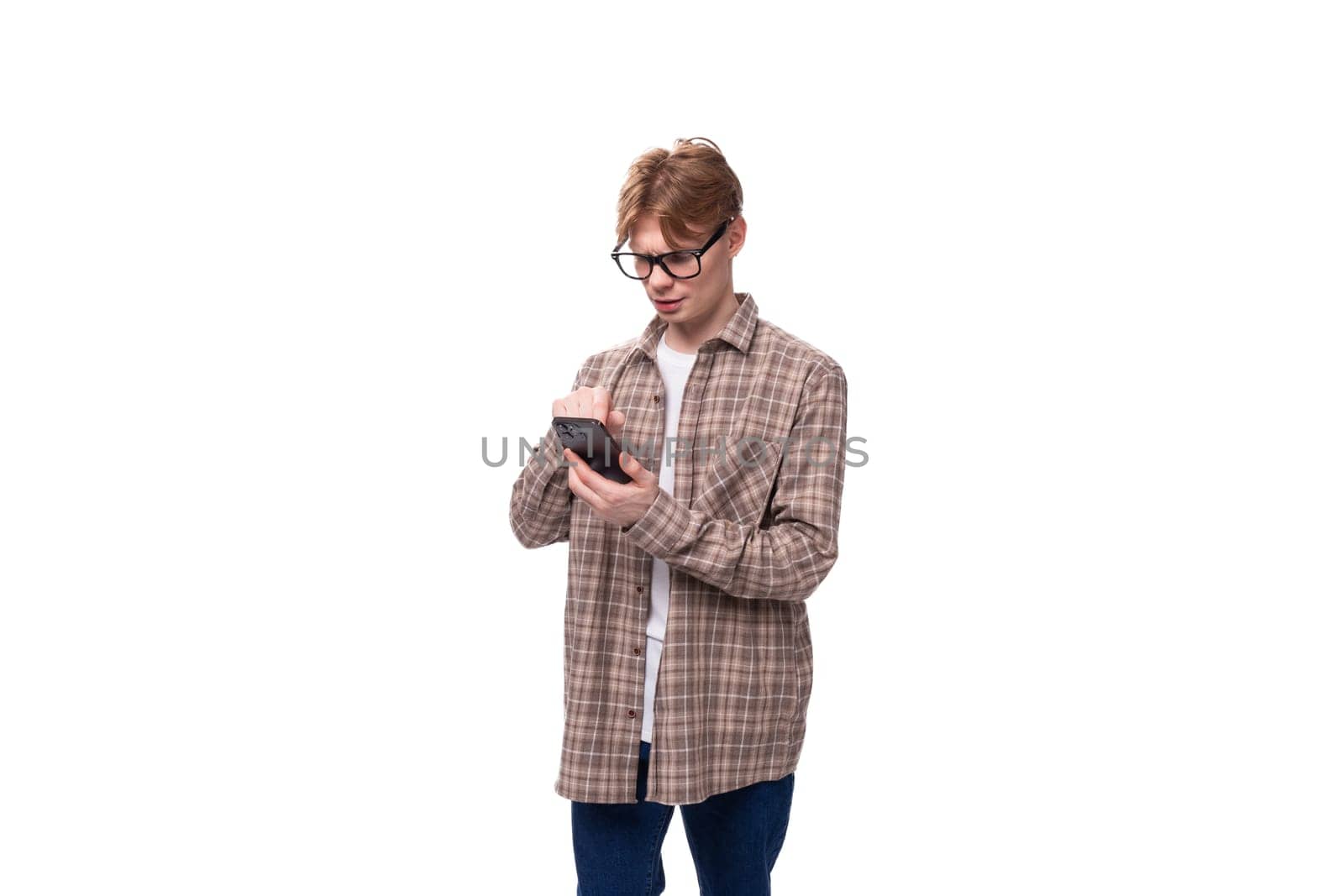 young caucasian guy with red hair in glasses and a plaid shirt communicates using a smartphone by TRMK