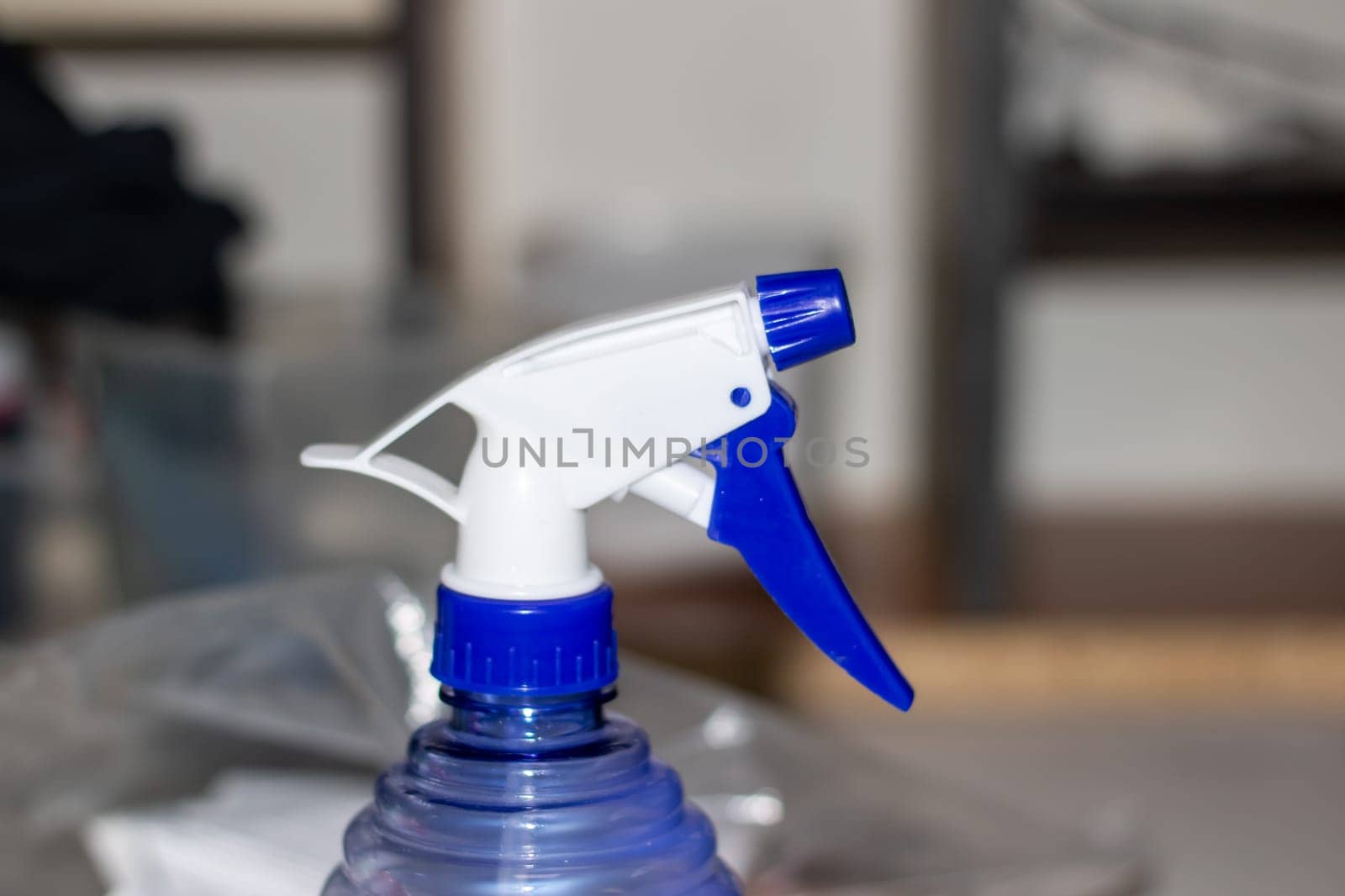 An electric blue and white spray bottle filled with liquid is resting on a table. The bottle contains a waterbased fluid, perfect for cleaning glass and plastic surfaces
