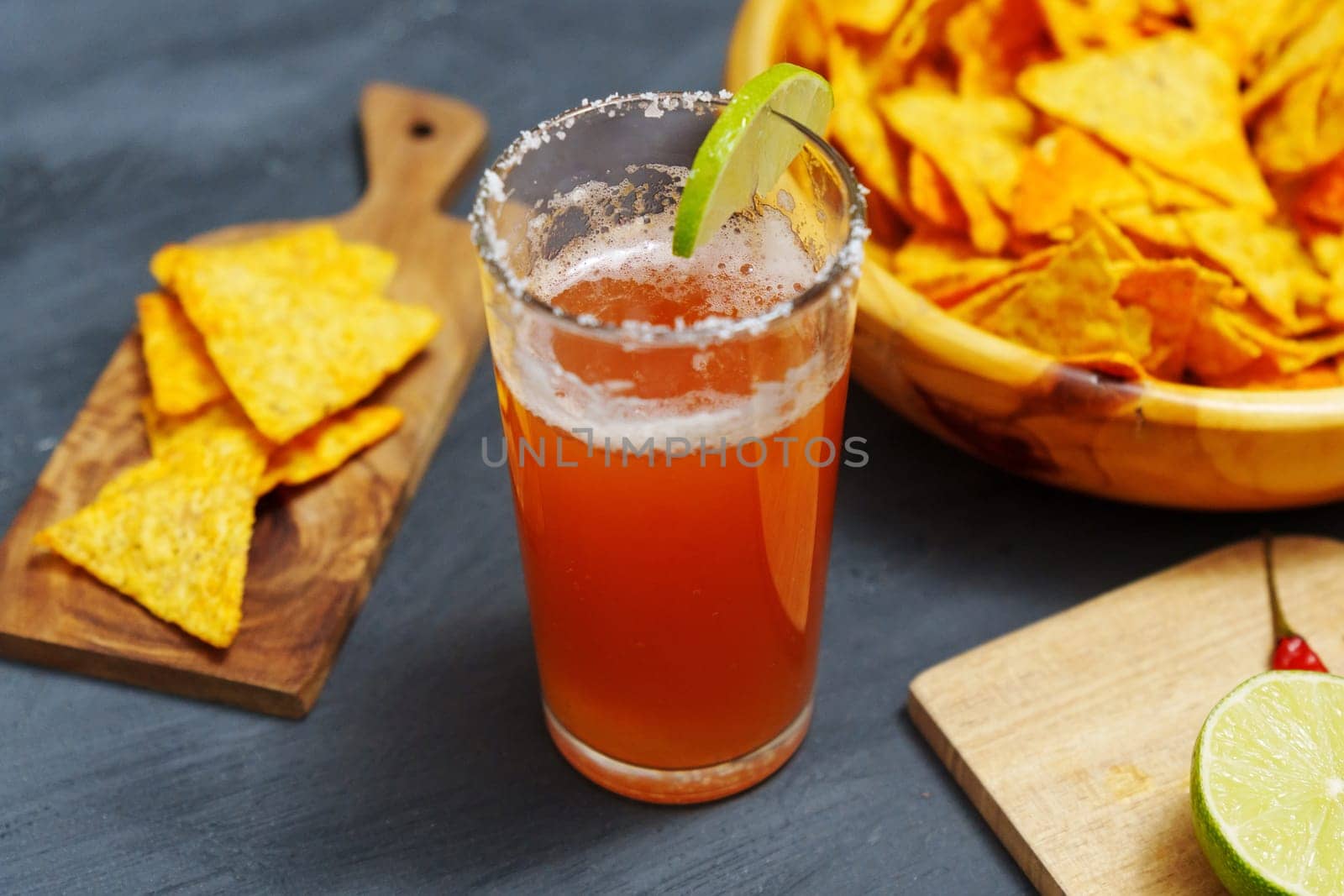 Michelada cocktail with tomato juice, beer and lime in a glass and nachos. Selective focus by darksoul72