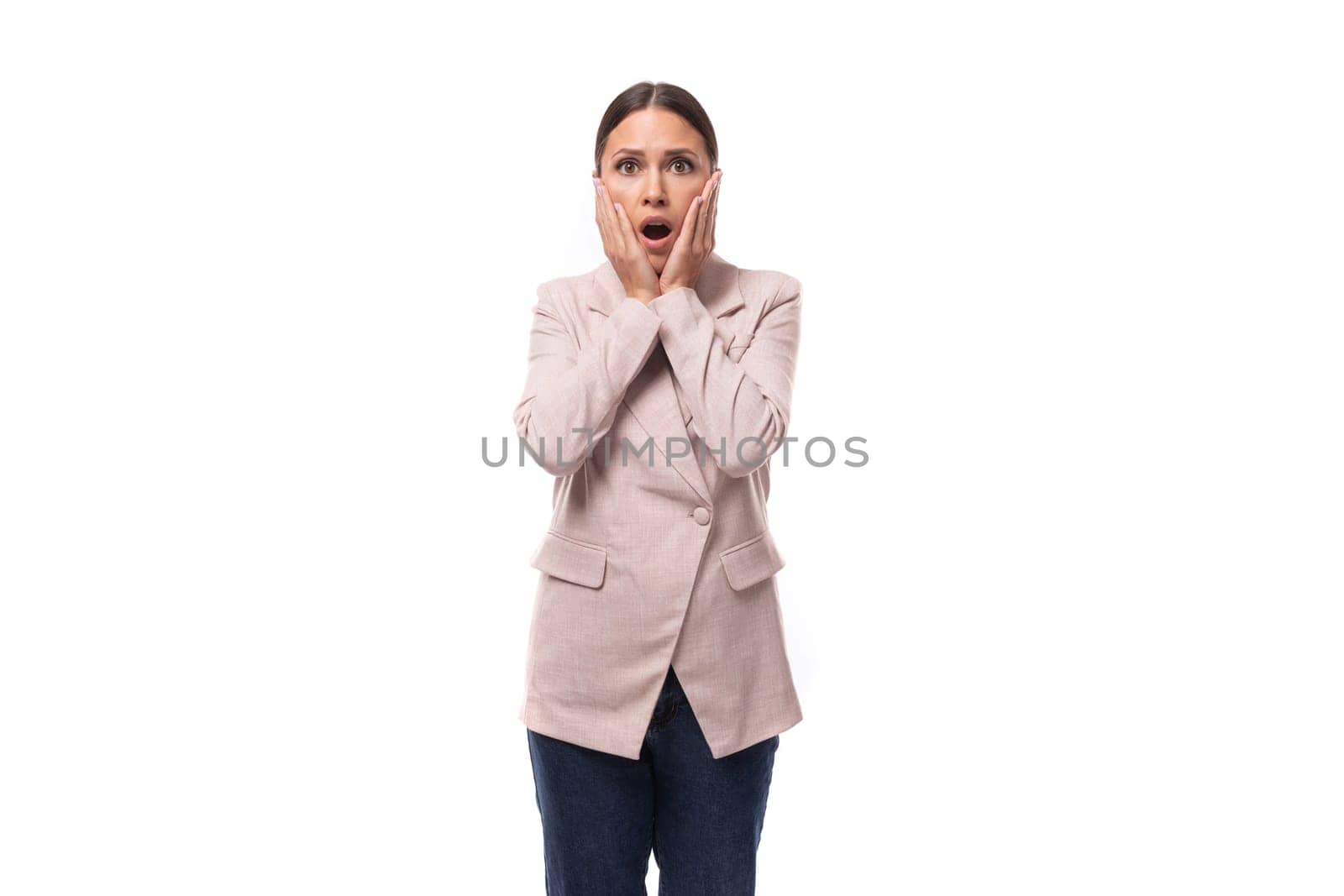 young well-groomed brunette woman dressed in a beige jacket looks at the camera in surprise on a white background with copy space by TRMK