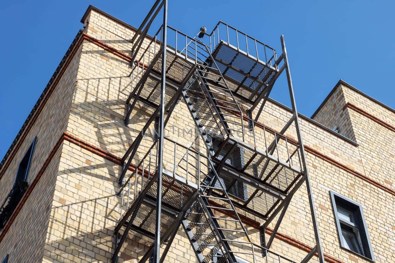 A fire escape made of wood is attached to the buildings facade in the city. It provides an escape route from the condominium through a window to the roof, avoiding overhead power lines