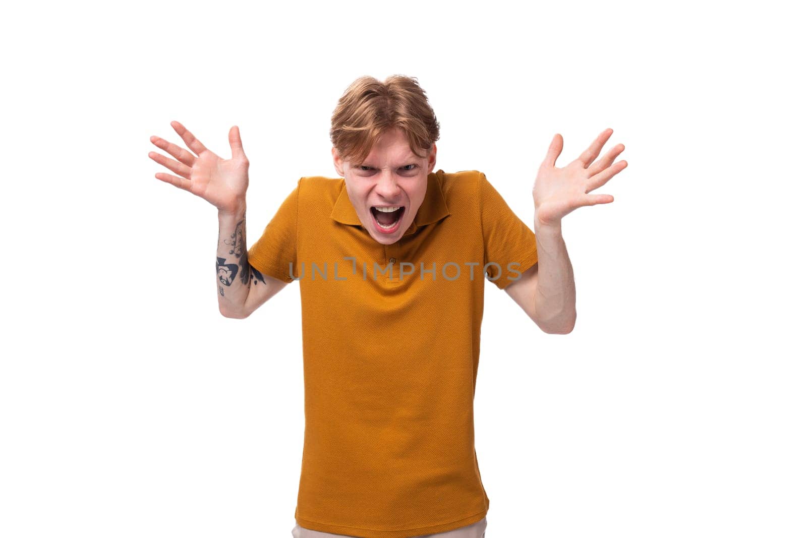 a young frustrated guy with short red hair dressed in a summer orange T-shirt is shouting with his hands up.