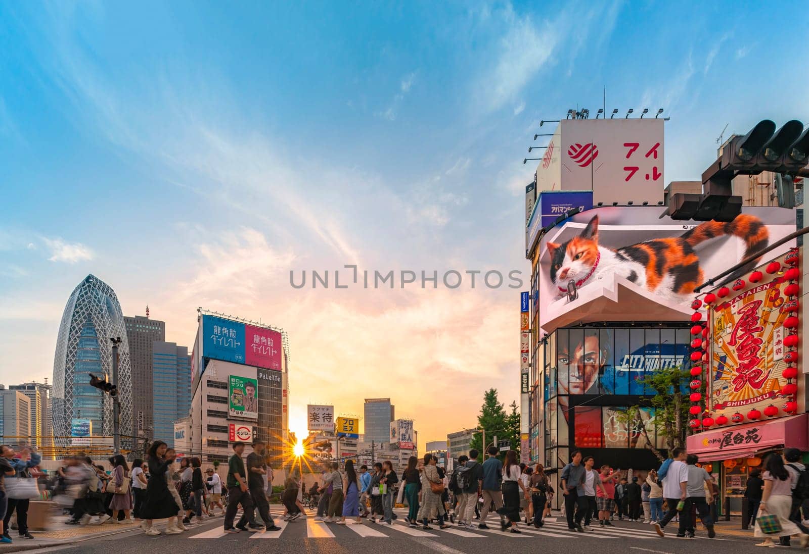 tokyo, japan - apr 28 2024: Sunset panorama of the Shinjuku East exit scramble crossing with the giant 3D cat of the Cross Shinjuku Vision building overlooking pedestrians and a poster of City Hunter.