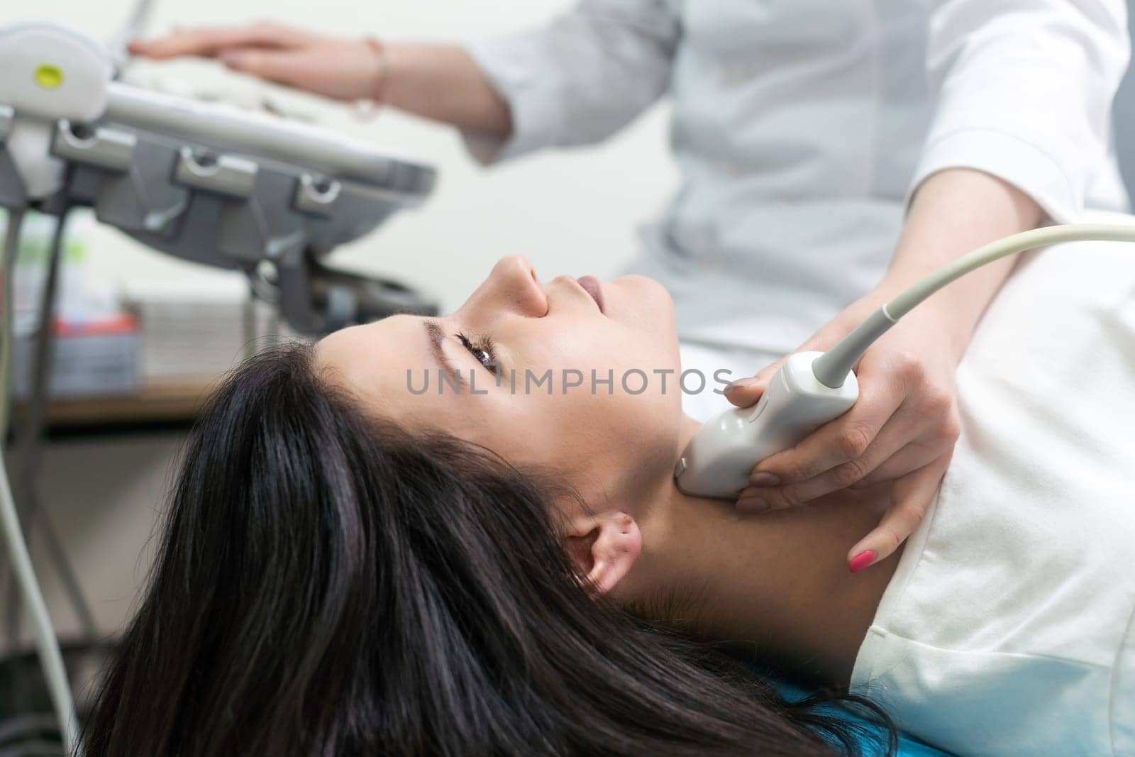 Doctor using ultrasound scanning machine for examining a thyroid of woman. by Andelov13