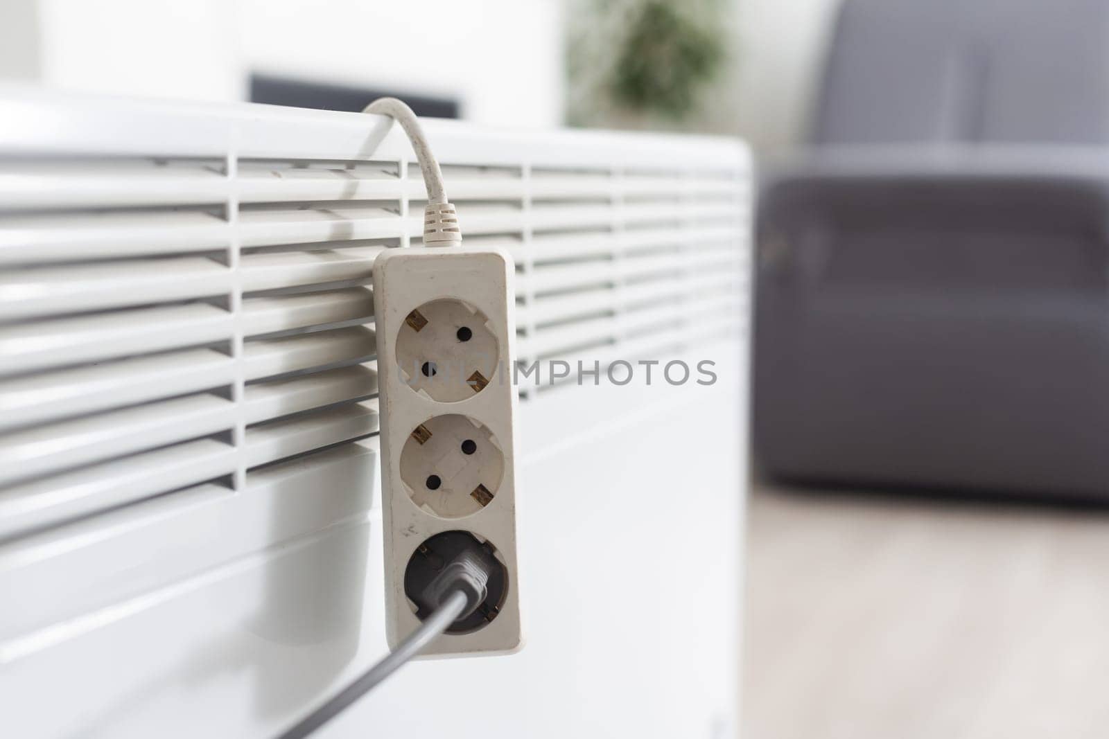 Electric heater plug inserted into extension cord. White radiator for home and office. House heating and comfort by Andelov13