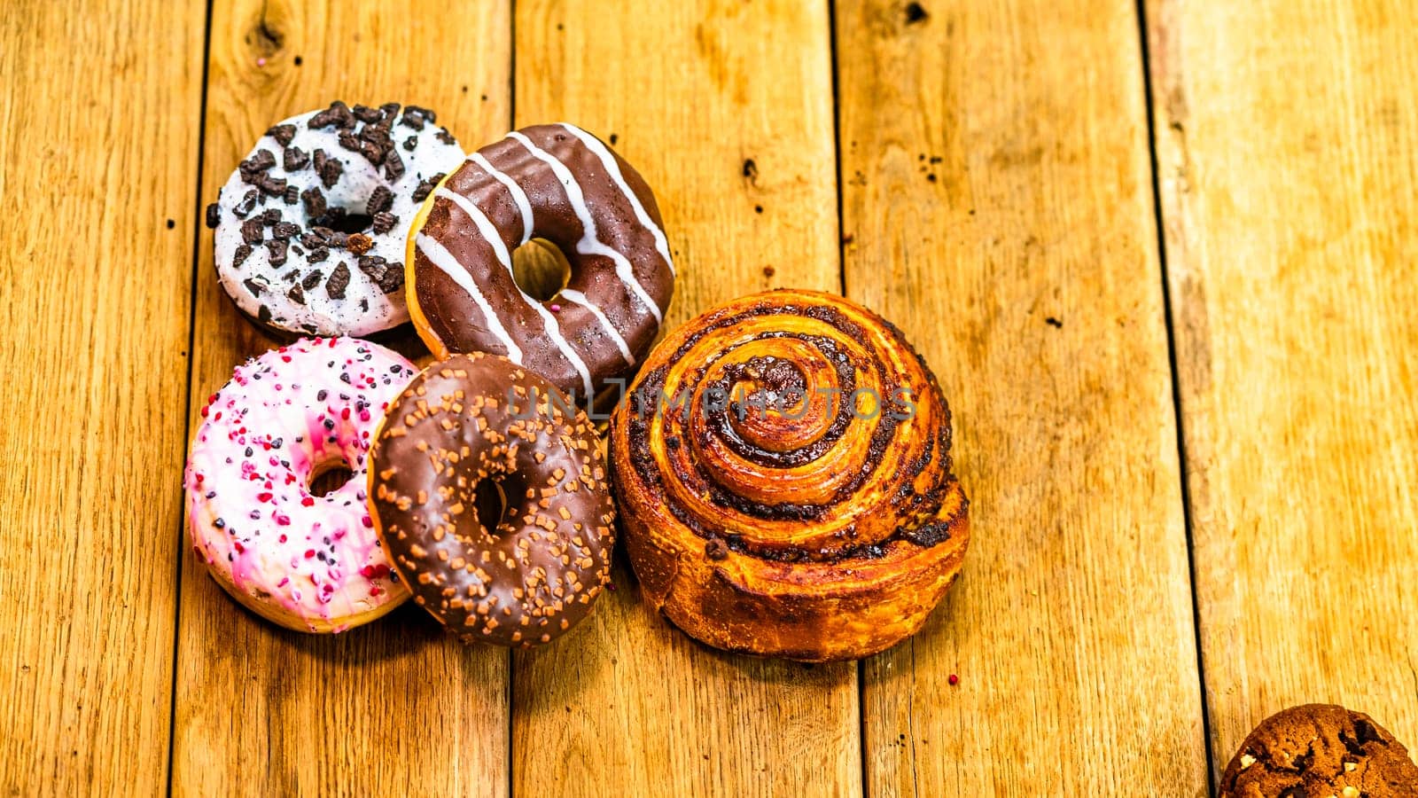 Colorful donuts, puff pastry and biscuits on wooden table. Sweet icing sugar food with glazed sprinkles, doughnut with chocolate frosting. Top view with copy space by vladispas