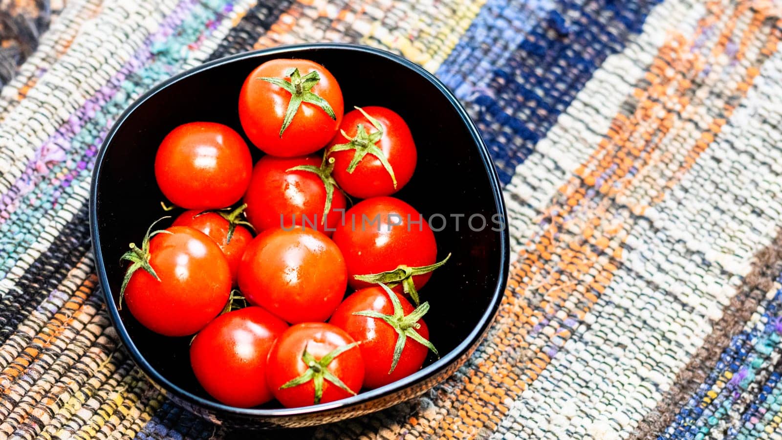 Detail of ripe cherry tomatoes in small black bowl on a rustic napkin. Ingredients and food concept by vladispas