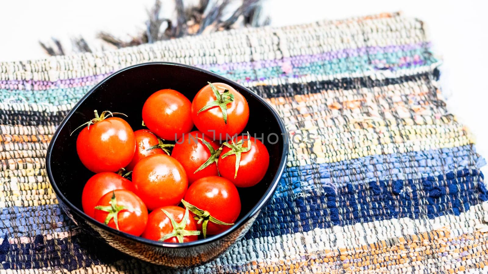 Detail of ripe cherry tomatoes in small black bowl on a rustic napkin. Ingredients and food concept by vladispas