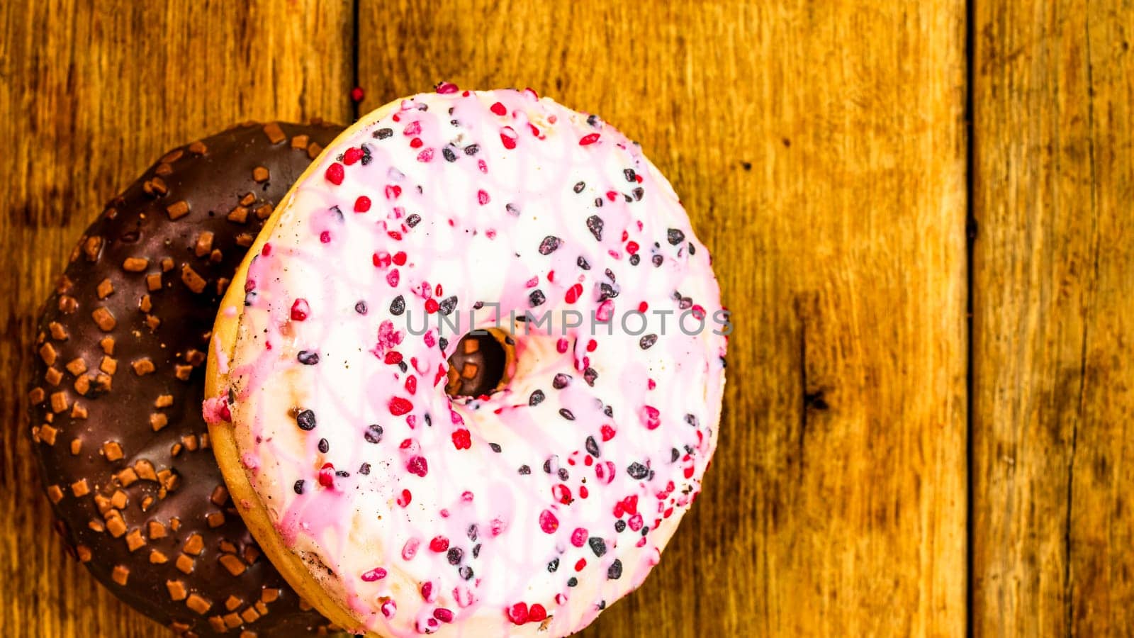 Colorful donuts on wooden table. Sweet icing sugar food with glazed sprinkles, doughnut with chocolate frosting. Top view with copy space