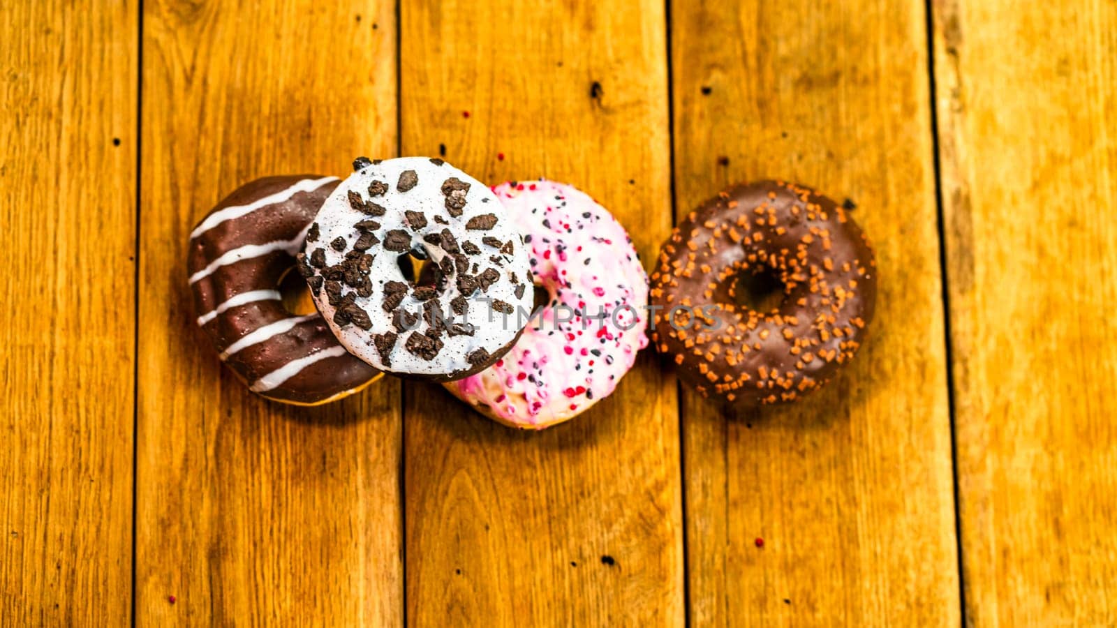 Colorful donuts on wooden table. Sweet icing sugar food with glazed sprinkles, doughnut with chocolate frosting. Top view with copy space