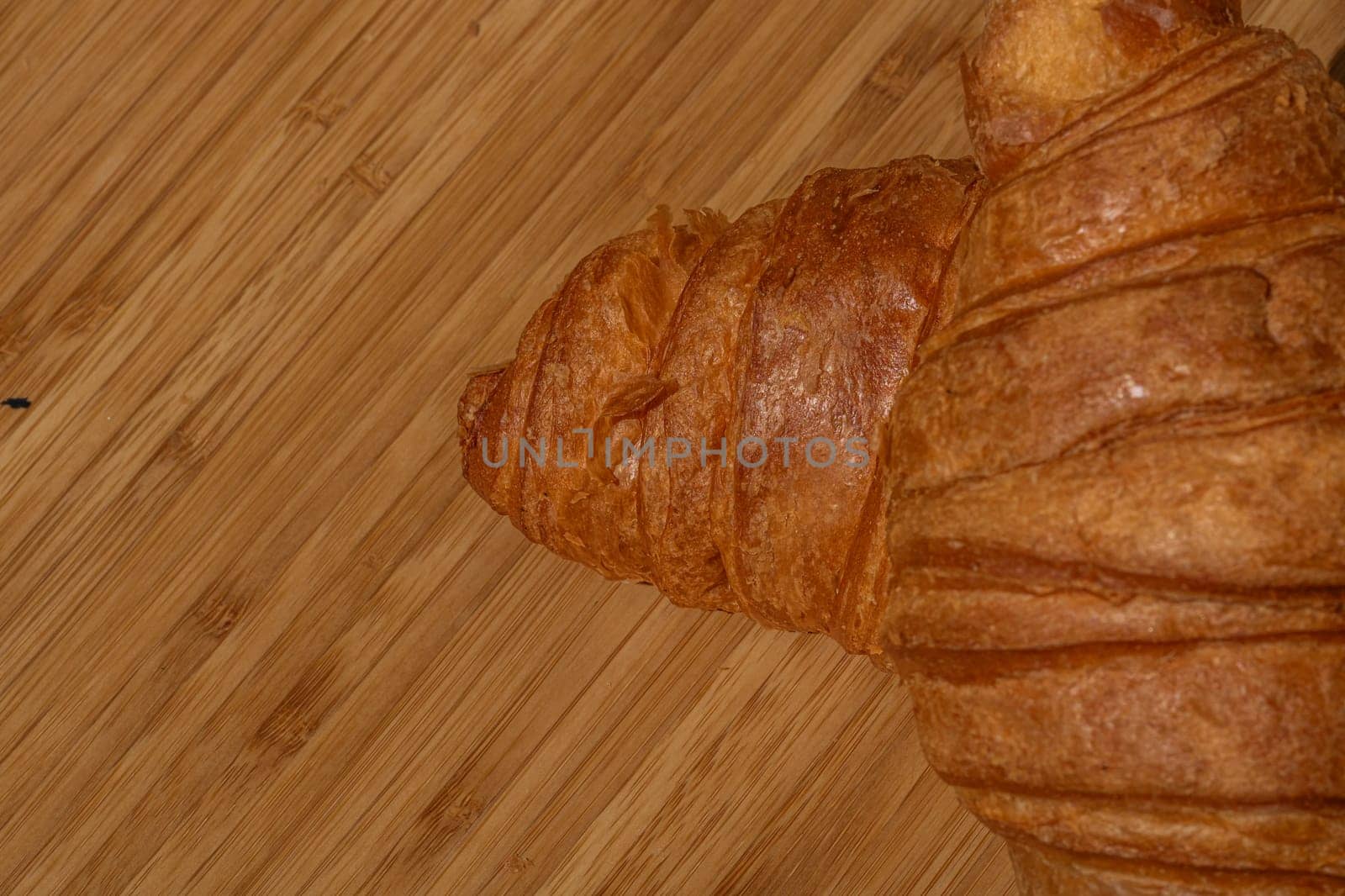 Detail of fresh croissant on wooden table. Food and breakfast concept. Close up photo of French buttery croissant  by vladispas