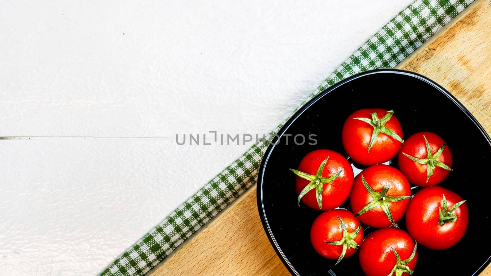 Top view of fresh ripe cherry tomatoes in small black bowl on a rustic white wooden table. Ingredients and food concept by vladispas