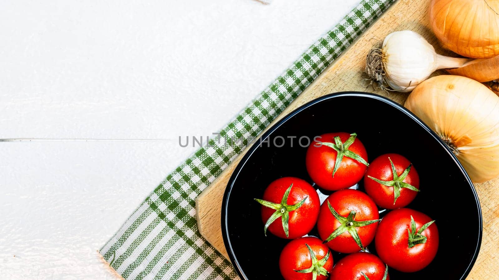Top view of onions, garlic and fresh ripe cherry tomatoes on a rustic white wooden table. Ingredients and food concept by vladispas