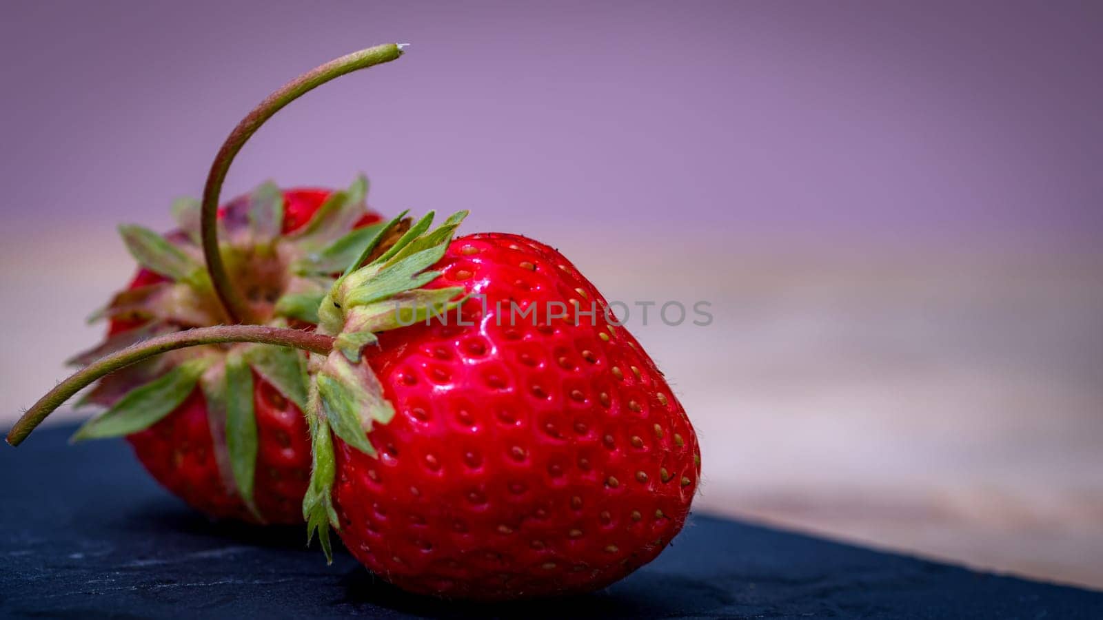 Close up of two strawberries on small black cutting board isolated outdoor on wooden table.