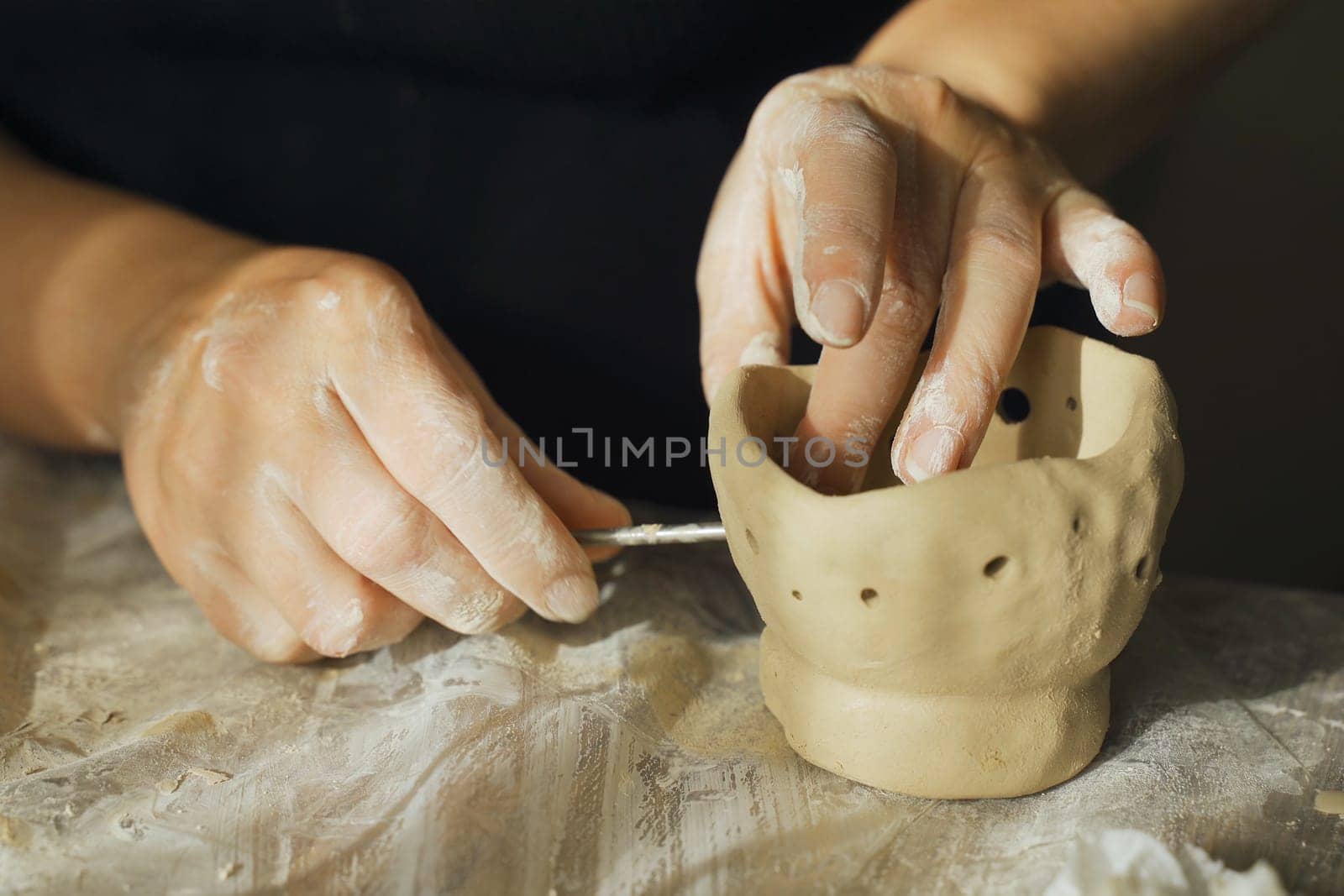 A woman makes holes using a tool in a clay craft - a candlestick. Close-up. Hobbies and creativity.
