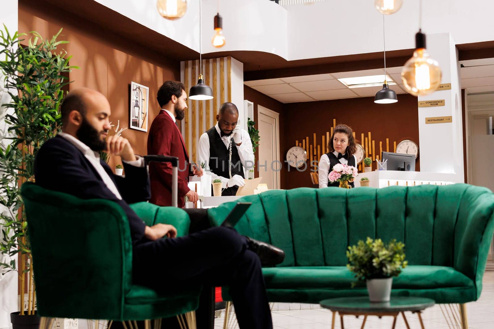 Businessman starting check in formalities, exchanging polite greetings with hotel receptionists at front desk. Company employee eager to see room and prepare for upcoming meetings.