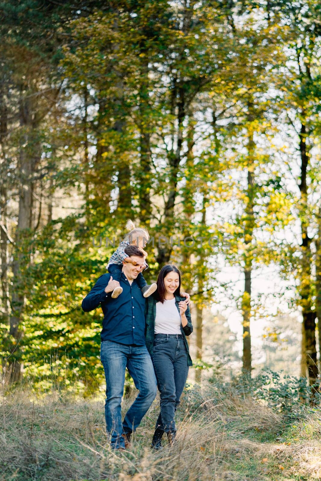 Dad with a little girl on his shoulders walks hugging mom in the park. High quality photo