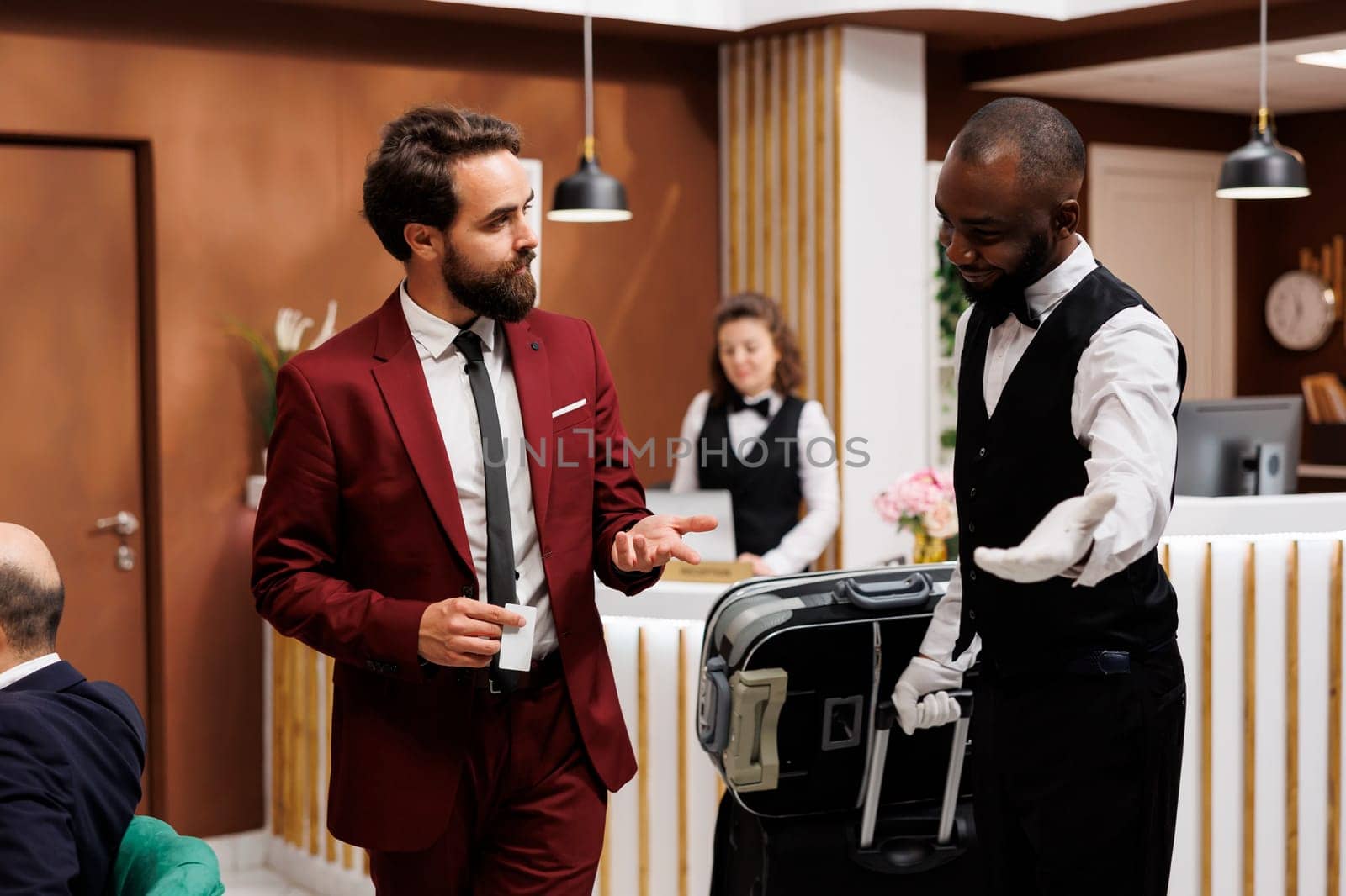 Bellboy taking guest to his hotel room, providing excellent luxury service for businessman with luggage. Bellhop carrying suitcase for traveller, formal client on business trip.