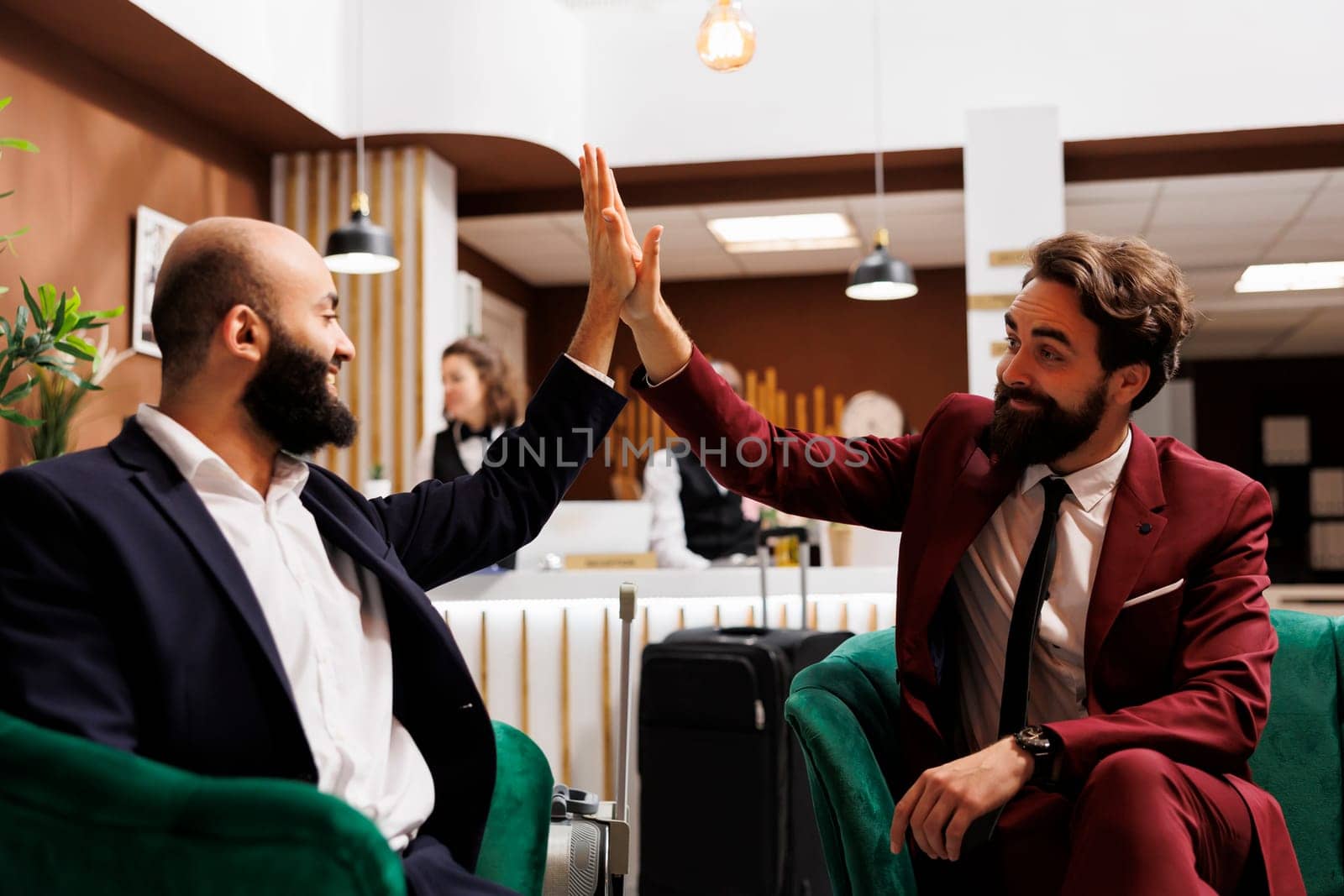 Business people team does highfive after successful international meeting, creating new corporate connections for development. Partners enjoying agreement, teamwork in hotel lobby.