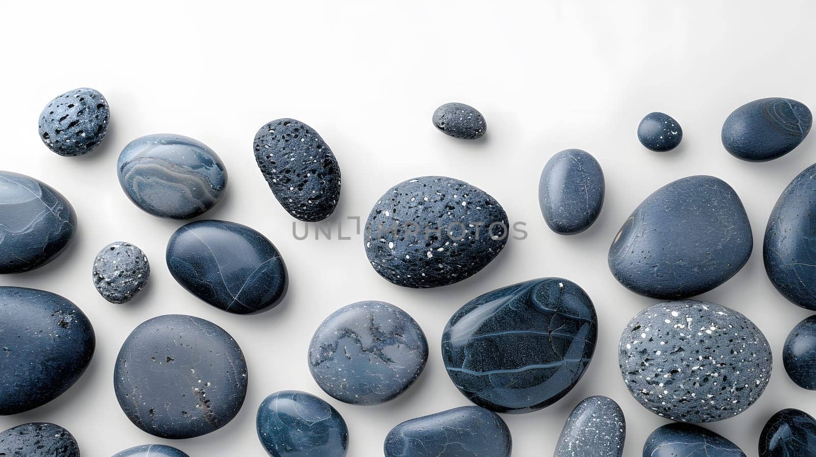 A collection of black rocks sits on a clean white surface, creating a striking pattern. Among the pebbles are electric blue circles resembling a fashion accessory or automotive tire