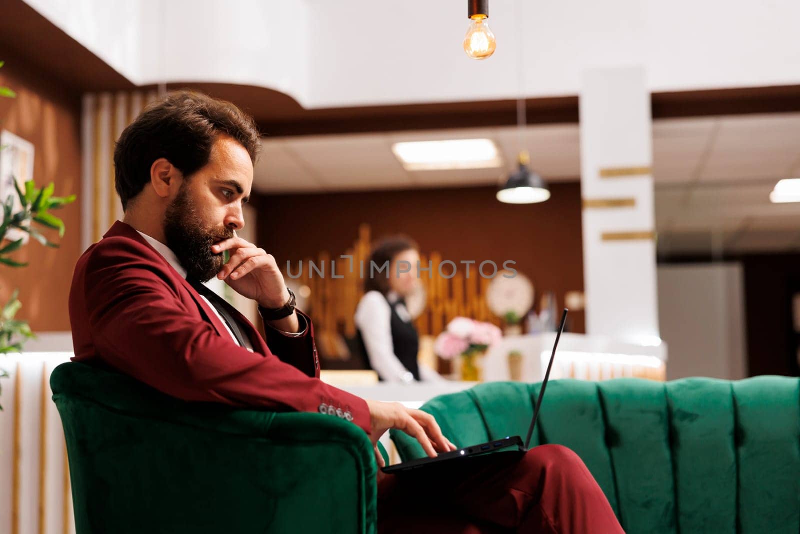 Company manager on business trip preparing to attend meeting in lounge area at hotel. Businessman waiting in reception lobby, checking presentation on laptop before starting conference.