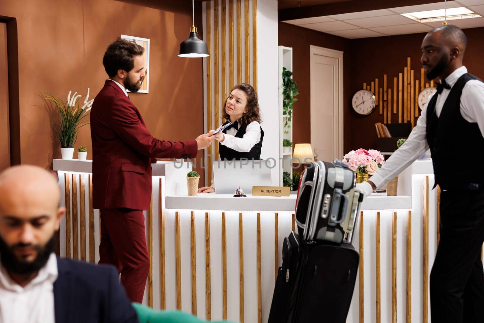 Formal guest fill in registration forms at front desk, doing easy check in process to see room reservation. Businessman travelling for work, receiving great concierge service from staff.