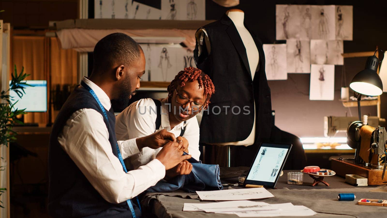 Two tailors choosing fabric for clothes in workshop, looking at materials on workstation before creating fashion collection. Team of couturiers crafting items with needlework.