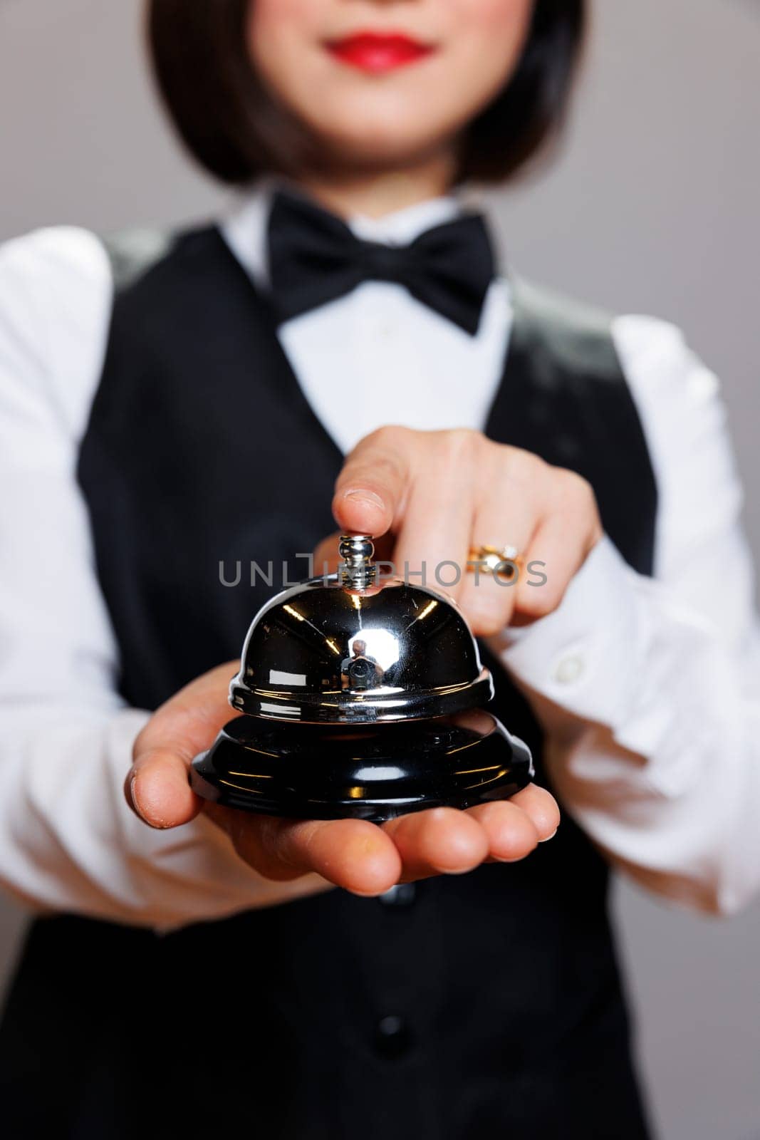 Waitress wearing professional uniform pressing hospitality bell with finger closeup. Restaurant woman receptionist holding dining alert, ringing and signaling about order