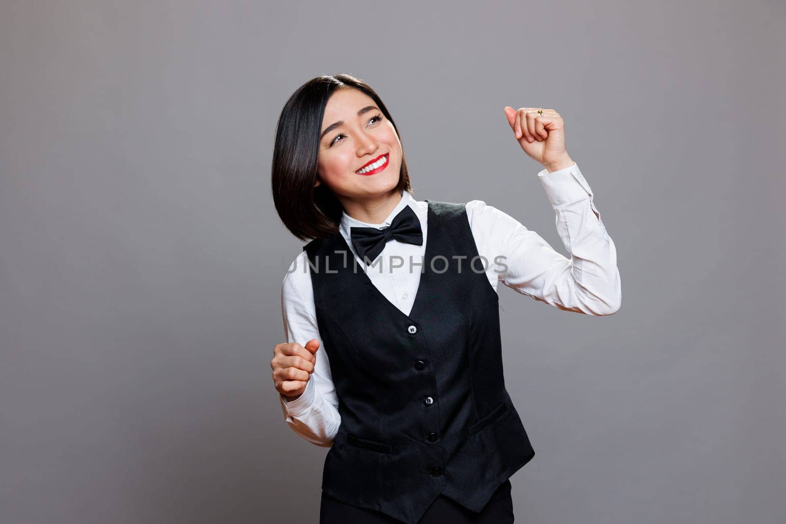 Attractive carefree asian woman receptionist wearing restaurant uniform joyfully dancing and having fun. Cheerful smiling young waitress moving arms to dynamic music beats