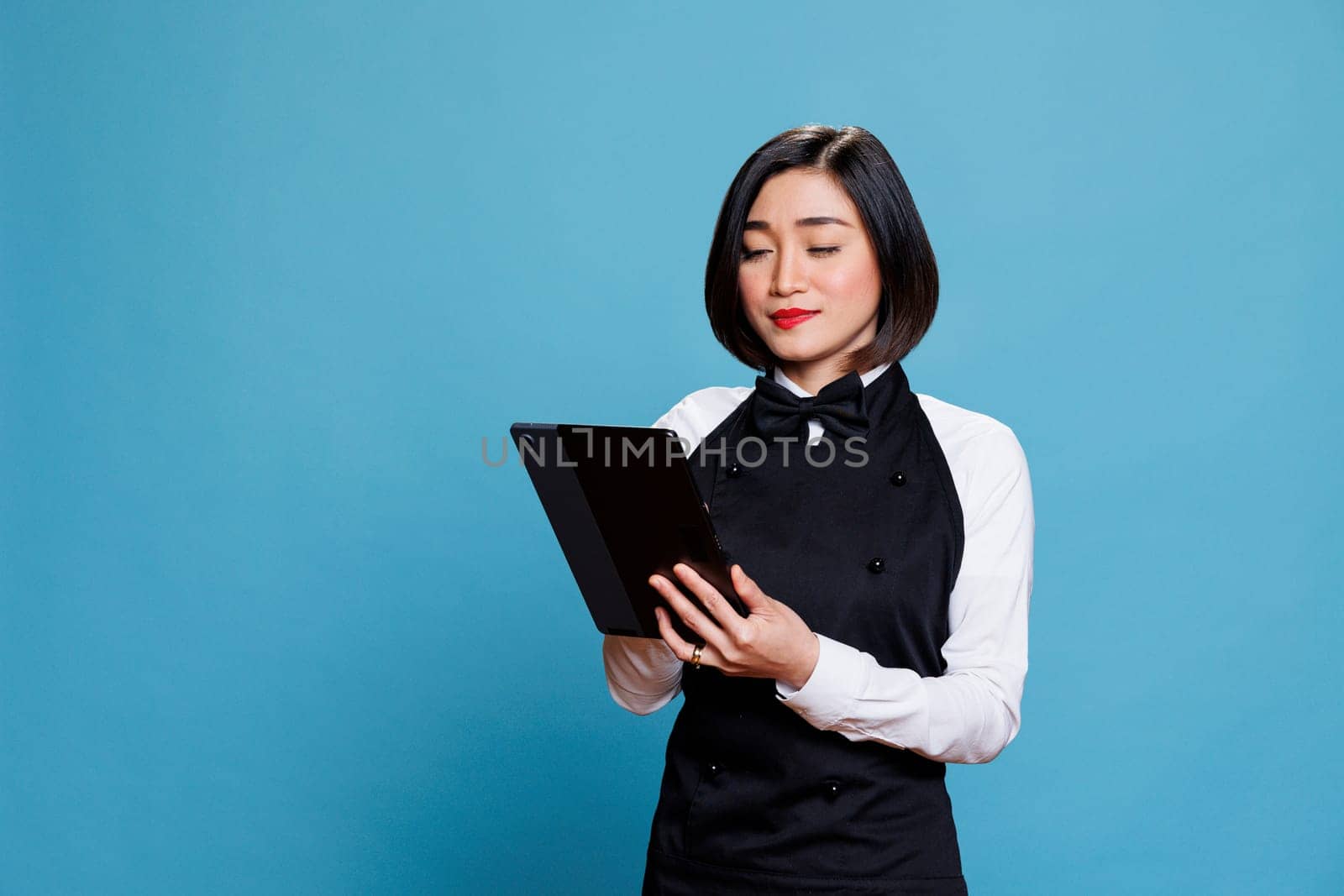 Restaurant young waitress using digital tablet while managing customer order online. Attractive hotel woman receptionist in uniform tapping on portable device touchscreen