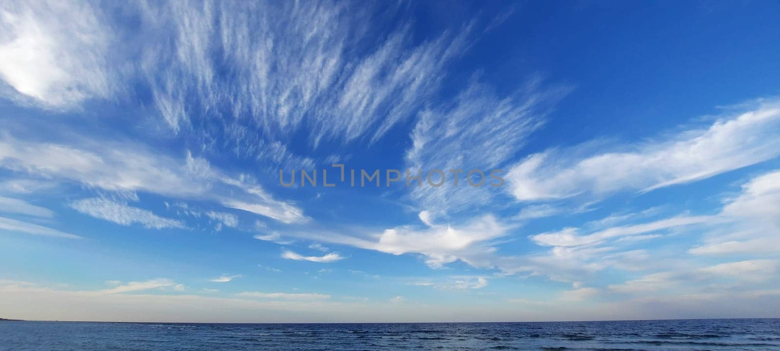 Red sea, Egypt. April 2024. Blue sea and sky background, blue shades horizon. White clouds on clear sky over sea water surface. Tranquil ocean with ripples. by Costin