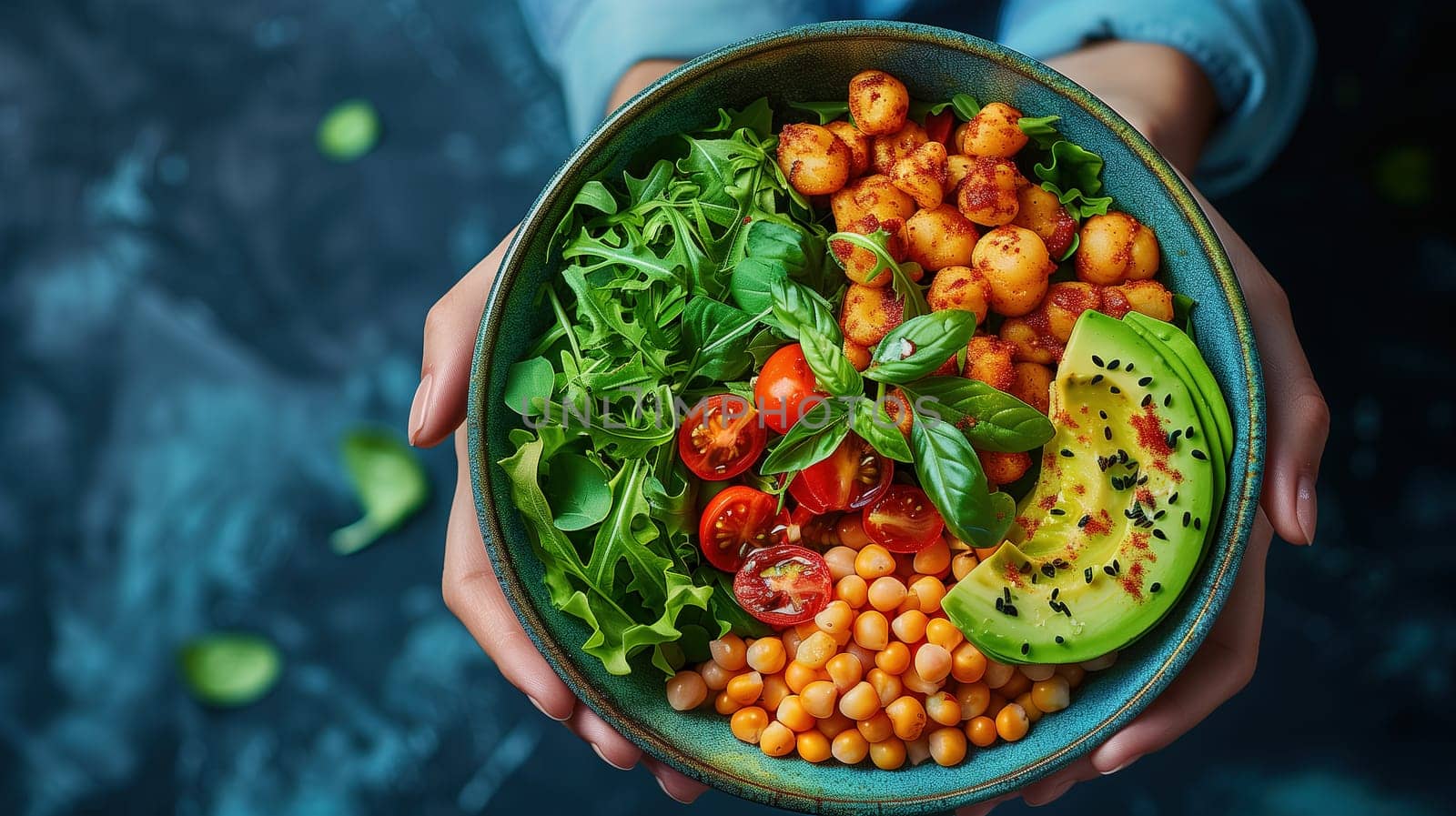 A person is holding a bowl filled with food, featuring avocado slices and chickpeas. The bowl is being held at waist level, showcasing a vibrant and nutritious meal.