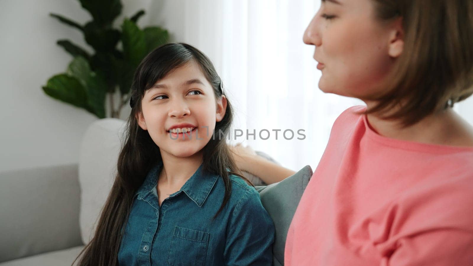 Happy mother sharing experience with daughter while sitting in living room. Caucasian mom and happy child talking and spend time together. Attractive girl listen parent story while smiling. Pedagogy.