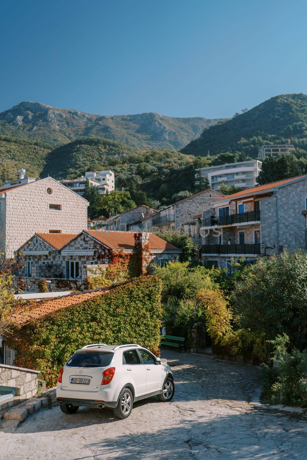 Car stands near a hedge near cozy apartment buildings at the foot of the mountains by Nadtochiy