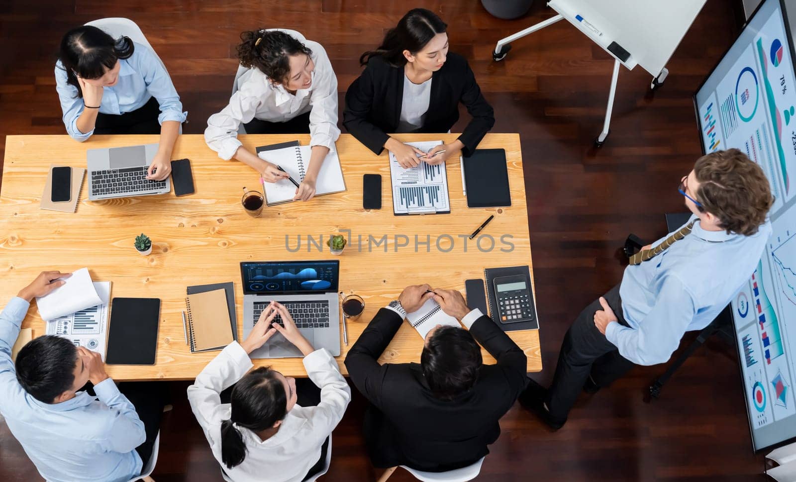 Wide top view of diverse group of business analyst team analyzing financial data report paper on meeting table. Chart and graph dashboard by business intelligence analysis. Meticulous