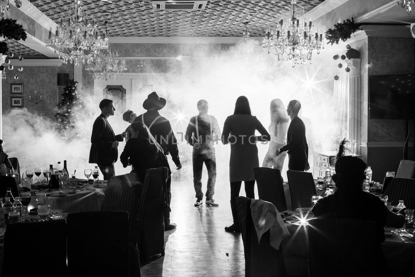 Corporativ Group of People dances in retro costumes. Silhouettes of dancing people at the disco in the clubYaremche, Bukovel, Ukraine - January 10, 2022 by malyshph