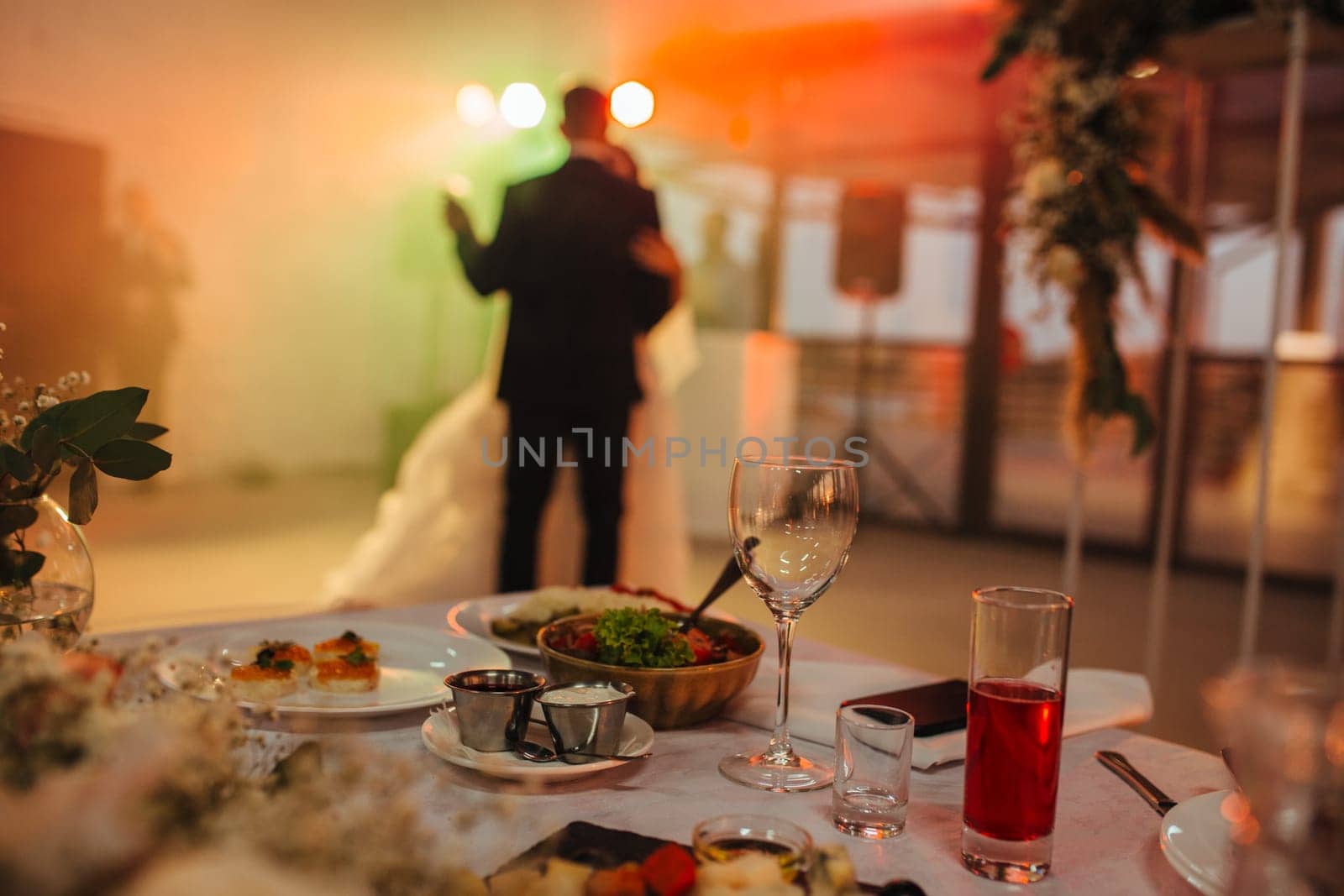 Selective focus on the wedding table with drinks and food in the background newlyweds dancing the first dance.