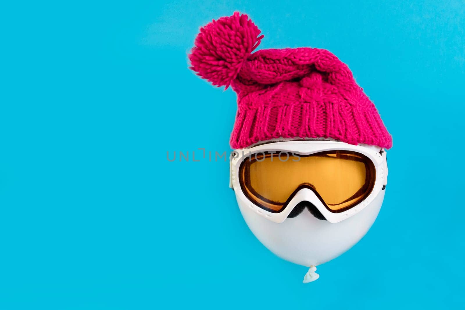Winter holidays. A balloon floating on a blue background wearing a ski mask and a winter hat. Concept of tourism and winter sports.
