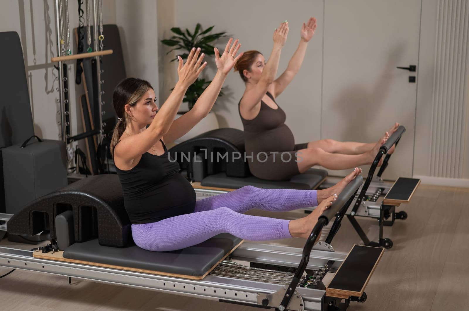 Two pregnant women do Pilates exercises on a reformer. Yoga class for pregnant women. by mrwed54