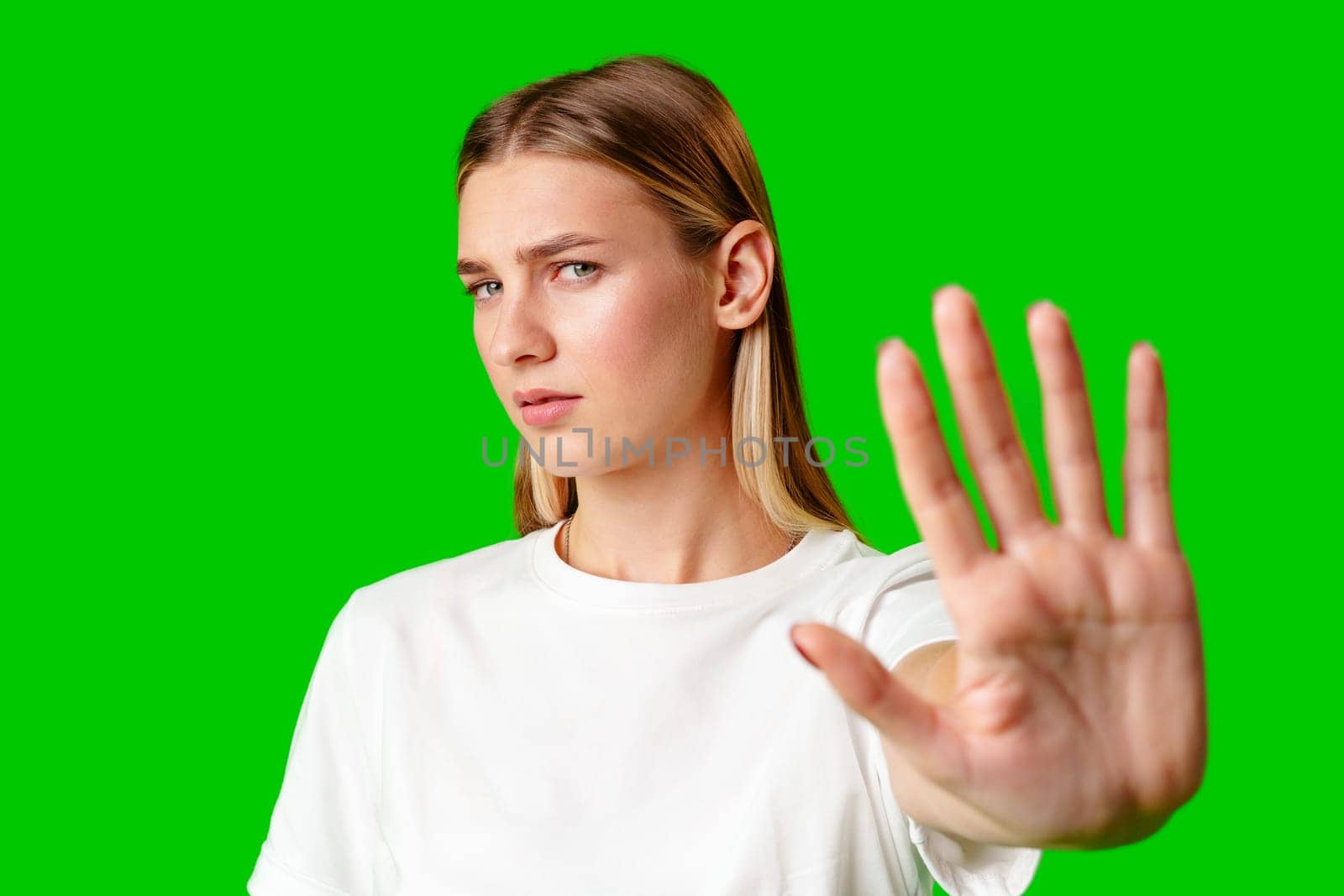 Young Woman Making Stop Sign Gesture on green background in studio