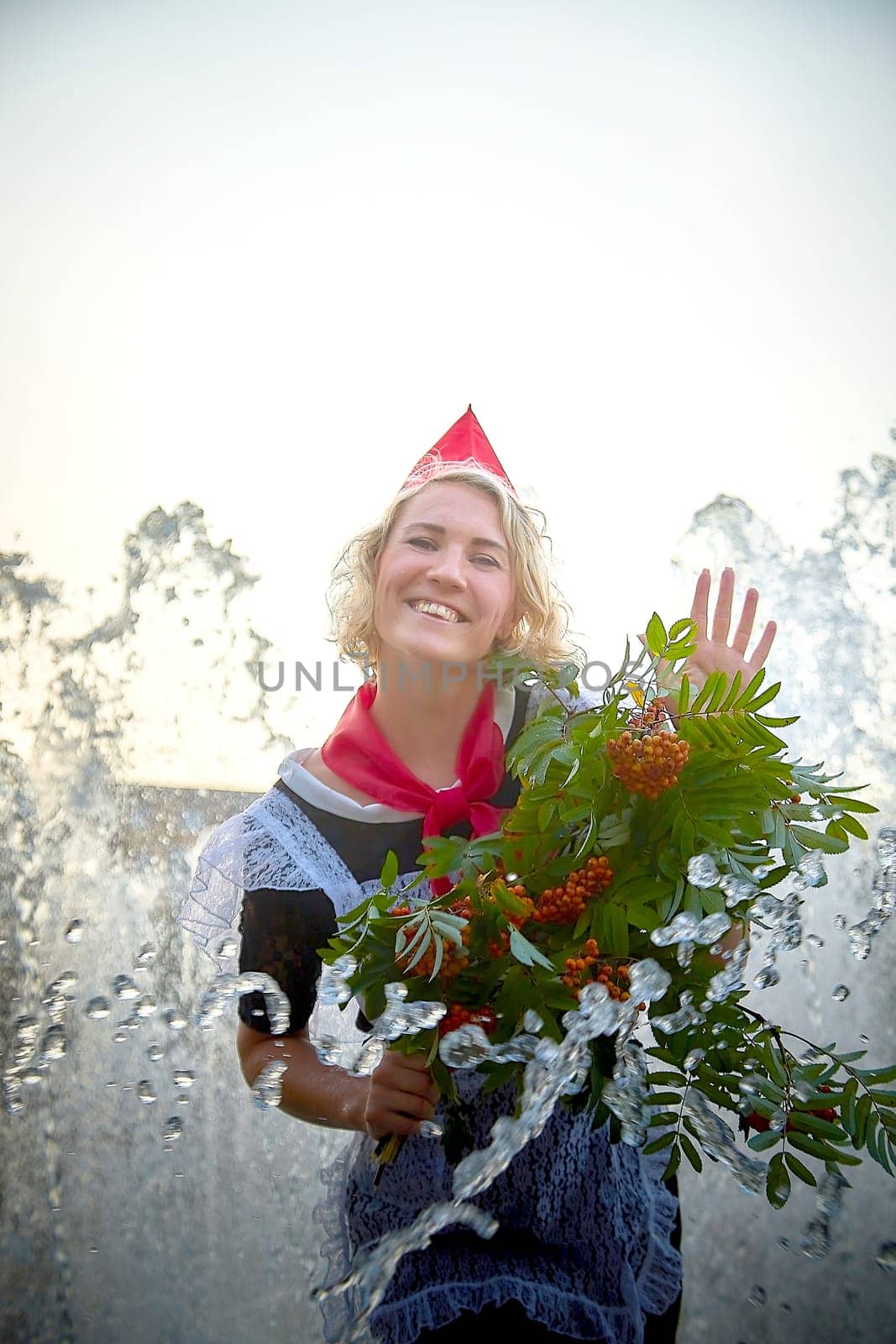 Girl in black school uniform, white apron and red tie near fountain water with bouquet of flowers. Nostalgia photo shoot of teenager of female pioneer from USSR costume for September 1 or graduation by keleny