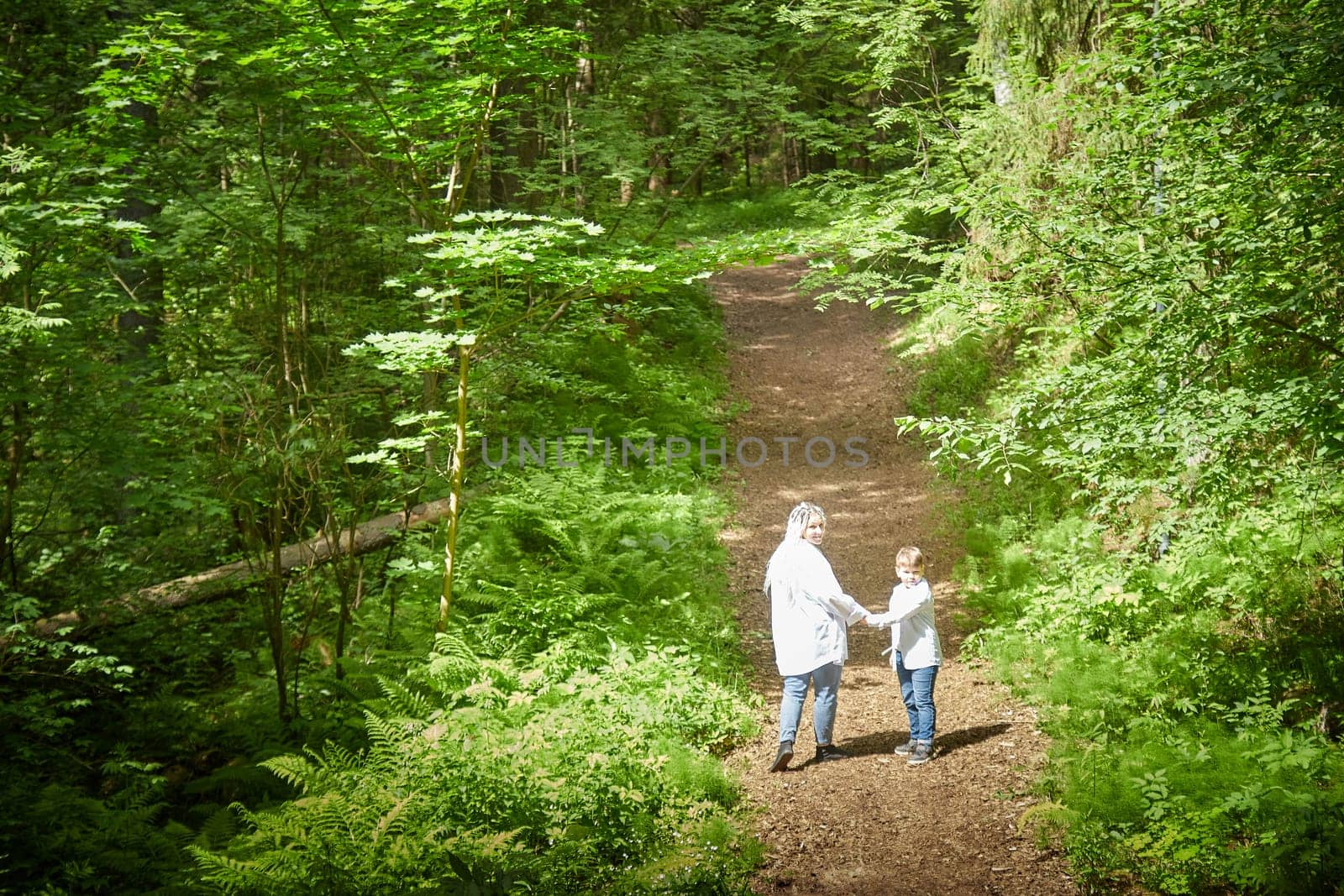 Funny mother with dreadlocks and fat boy happy walking in the woods on a sunny summer day by keleny
