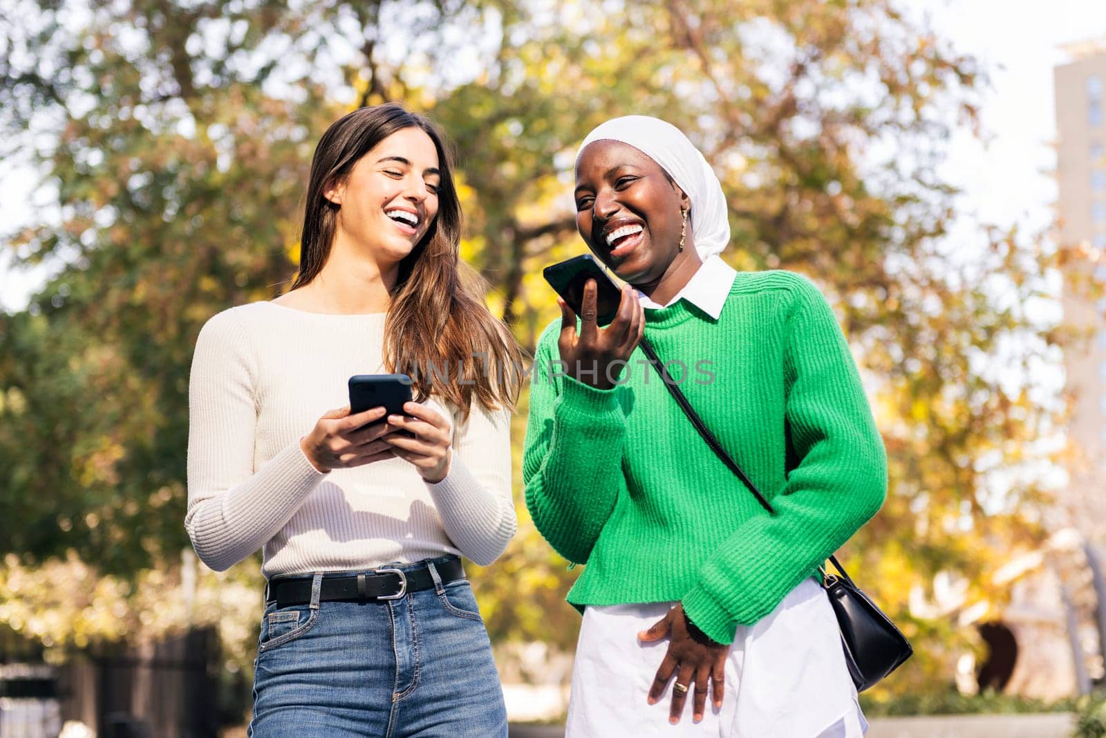 two young female friends laughing happy using their mobile phones, concept of friendship and technology